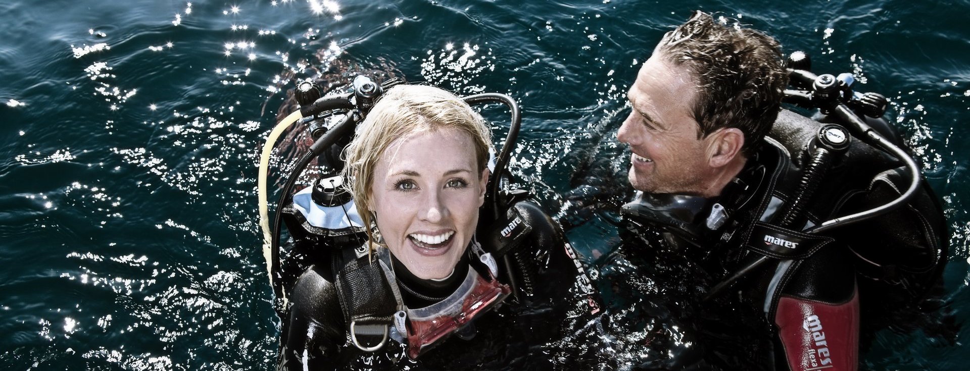 Deux plongeurs souriants à la surface de l'eau, profitant d'une expérience de plongée conviviale et sécurisée. Idéal pour les amateurs de plongée et les moments partagés.